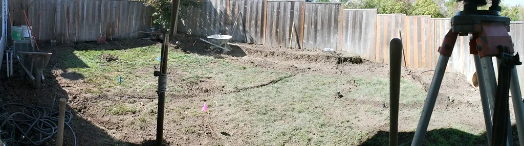 Gloved hands mark fill height above bedding in a trench with gravel and compacted soil layers