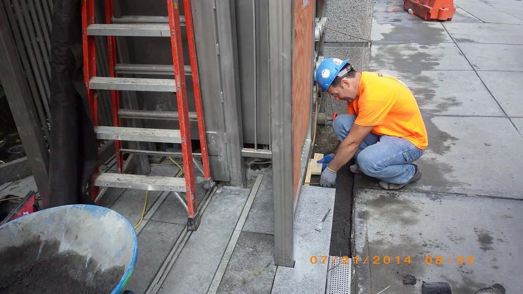 Hands screeding bedding sand over a compacted base with concrete pavers nearby