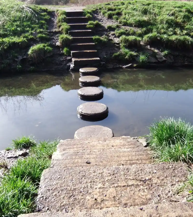 Hand measuring spacing between stepping stones on a gravel base